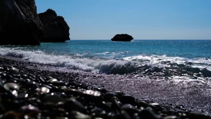 在圆石滩上滚滚的泡沫波浪在阳光下的石头特写镜头。蓝色地中海海水撞击岩石。海景，度假村，自然，夏天。