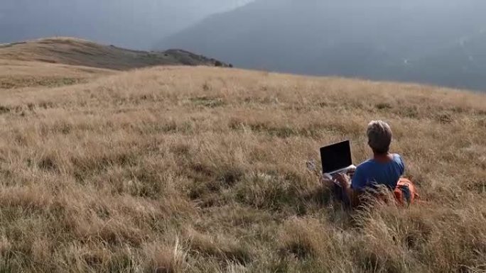 男子在草地山坡上使用笔记本电脑