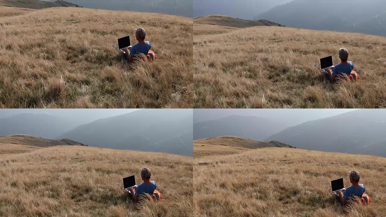 男子在草地山坡上使用笔记本电脑
