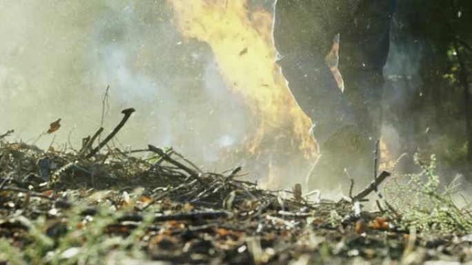 一个四十多岁的高加索人在户外用干草叉将木棍和树枝扔到一个大的燃烧燃烧堆上