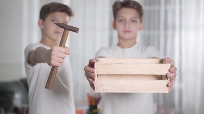 可爱的高加索双胞胎兄弟的肖像展示木制品和锤子，并开始快乐地跳舞。焦点从背景到前后变化。木工，儿童木工