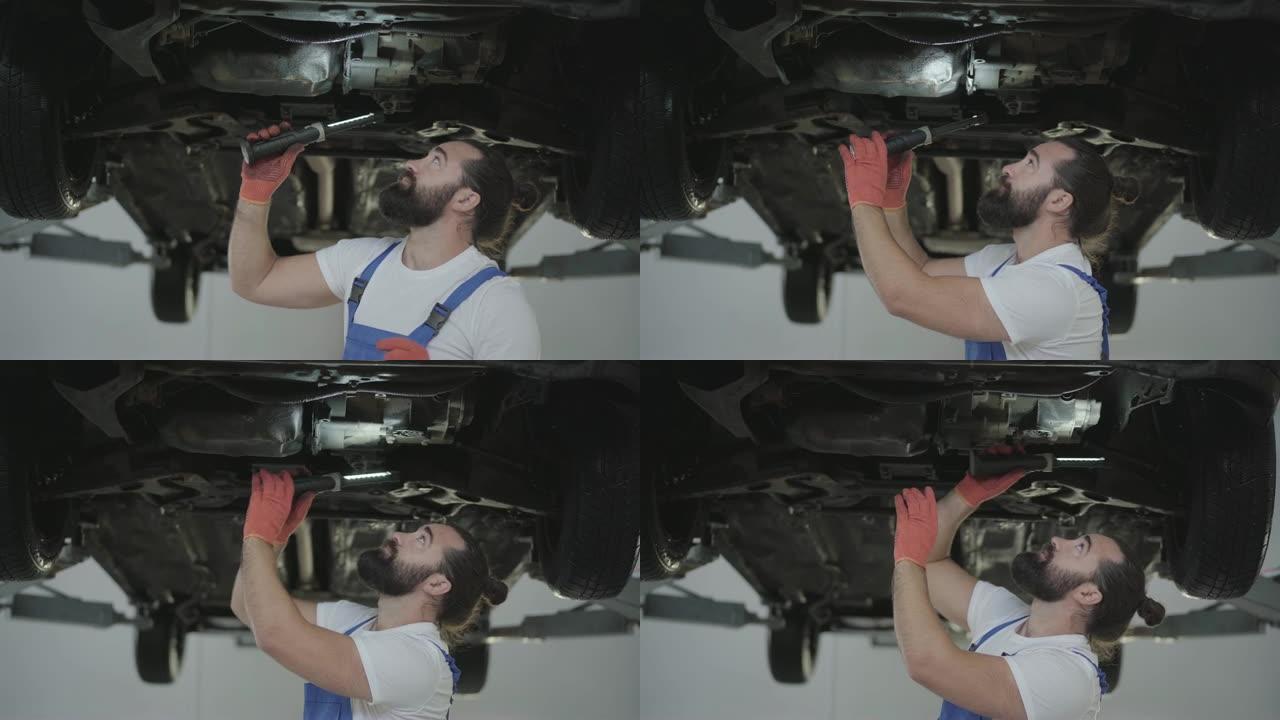 成功的胡须机械师在维修服务站用举升汽车的手电筒检查汽车的悬架或制动器。