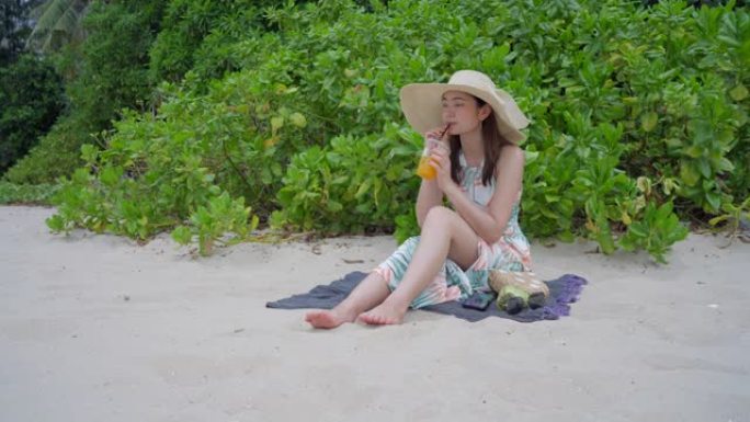 美丽的女人在海滩上喝橙汁。