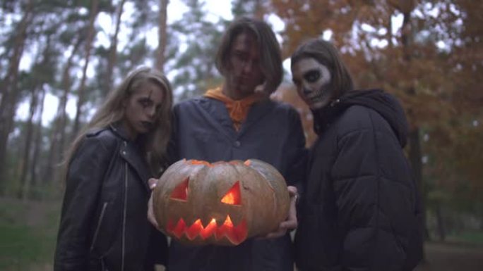 高大英俊的男人拿着万圣节南瓜，里面有一盏灯，两个漂亮的女孩站在附近。