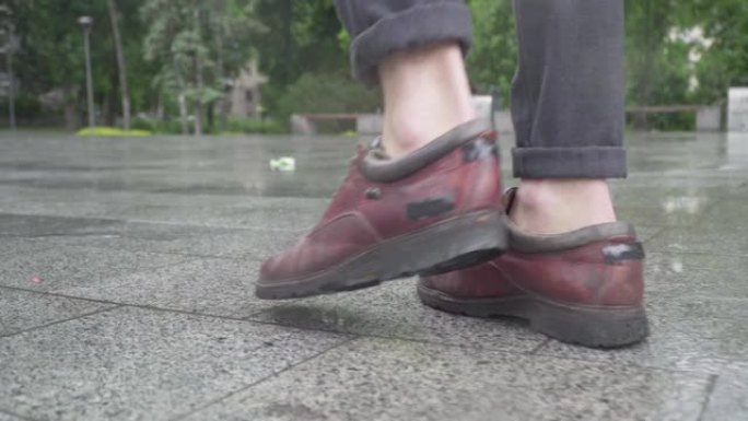 相机跟随优雅的白人年轻人的脚步。穿着靴子的男性脚在城市街道的人行道上行走的特写镜头。无法辨认的男人在
