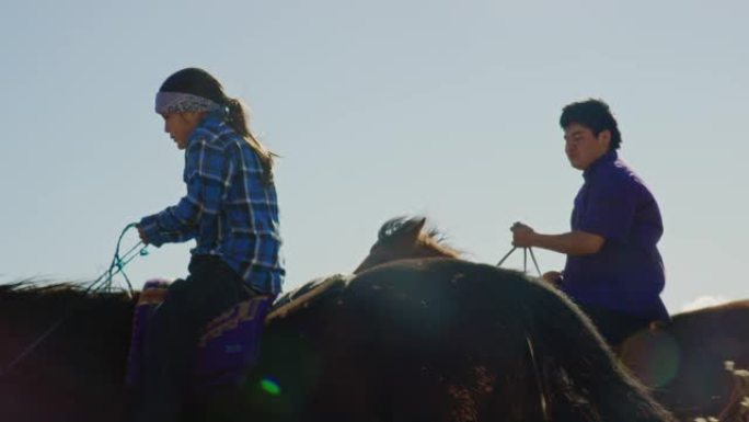 在晴朗，明亮的日子里，几名年轻的美国原住民 (纳瓦霍人) 儿童骑着马穿过亚利桑那州/犹他州的纪念碑谷