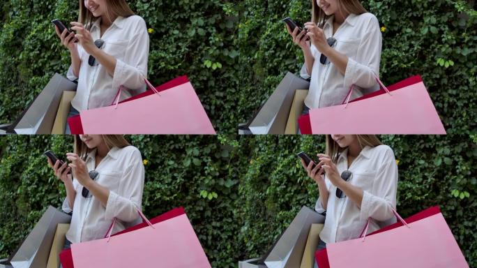 4k镜头慢动作美女走到商场外面她正在用手机，提着购物袋是五颜六色的，她很开心。买了她喜欢的东西