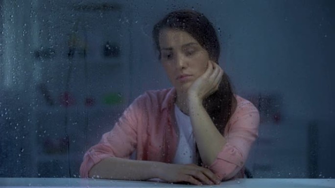 沉思的女人透过下雨的窗户，思考生活问题