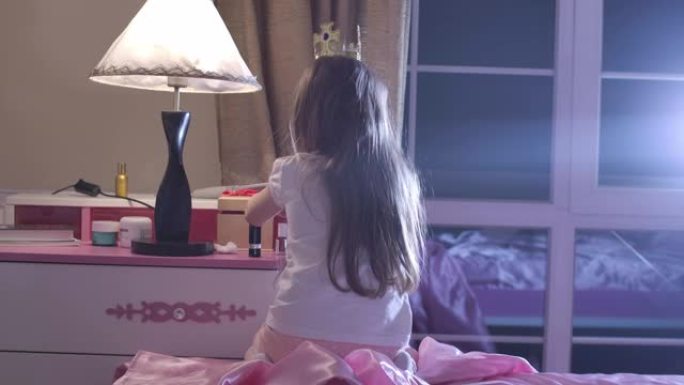 十几岁的白人女孩坐在粉红色的床上，头上戴着玩具皇冠。小学生准备睡觉。童年，休息，就寝时间。电影院4k