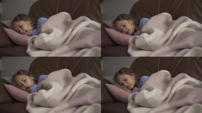 生病的年轻白人女孩躺在家里的毯子下咳嗽。这孩子有发热。