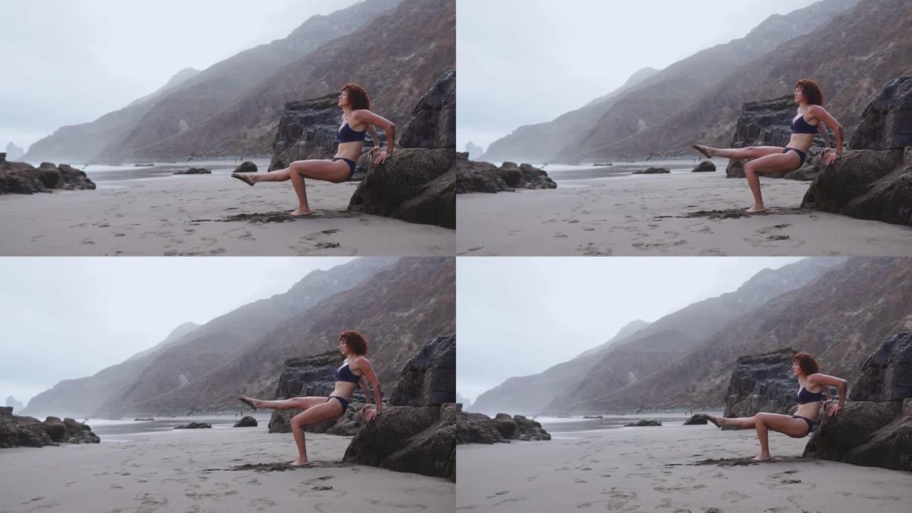 女人在海边的一块岩石上做俯卧撑。健身年轻女子在海滩上俯卧撑