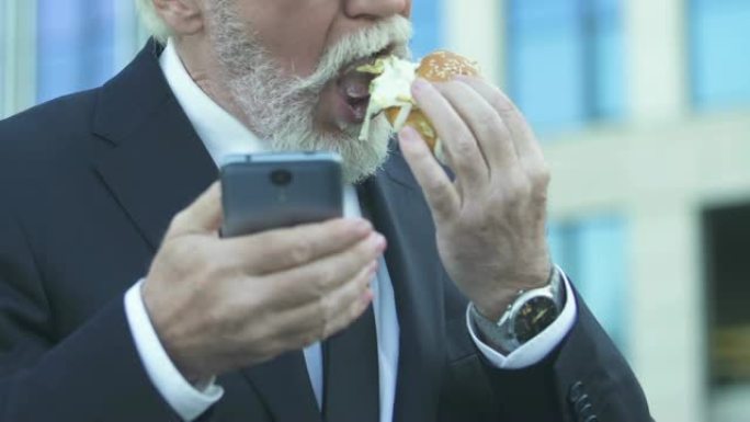商人在使用电话时吃汉堡，由于忙碌的生活方式而导致营养不良