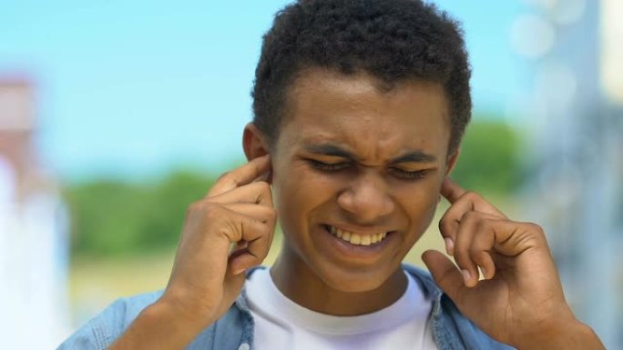 十几岁的男孩因疼痛而闭上耳朵，遭受嗡嗡声，听力受损