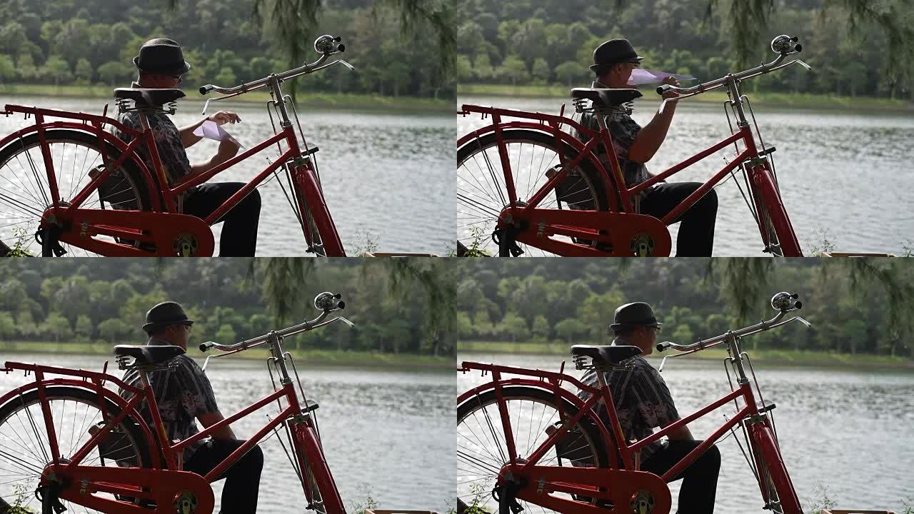 该名男子坐在自行车旁，在湖边扔纸飞机。