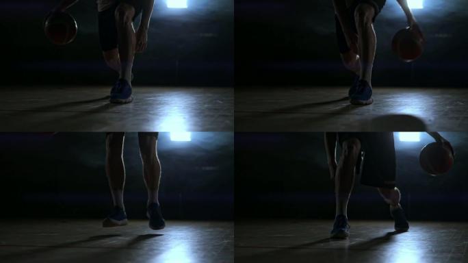 运球篮球运动员在黑暗的房间里的特写镜头在慢动作中