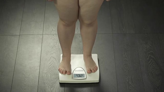 超重的女性踩在浴室秤上，健康失调，肥胖