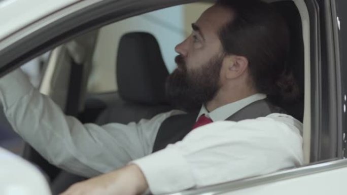 肖像迷人的自信的大胡子商人坐在车里，从汽车经销店检查新购买的汽车。