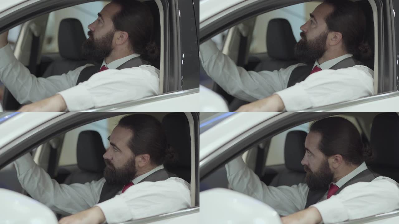 肖像迷人的自信的大胡子商人坐在车里，从汽车经销店检查新购买的汽车。