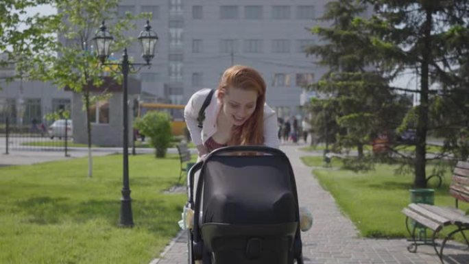 美丽的女人弯下腰在公园的婴儿车上。