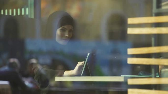 美丽的穆斯林女性坐在咖啡馆，在平板电脑上使用购物应用程序，银行
