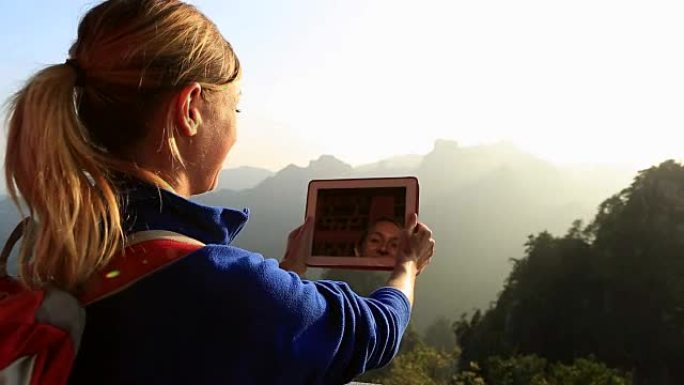 山顶上的女徒步旅行者拍摄数字平板电脑图片