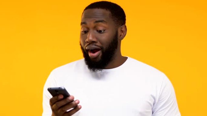 惊讶的黑人男子看着智能手机，手机应用程序更新，黄色背景