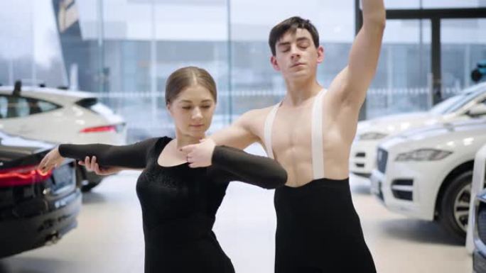 专业的高加索芭蕾舞演员用手做动作，看着相机，微笑着。自信的男人和女人在汽车经销店跳舞经典舞蹈。汽车工