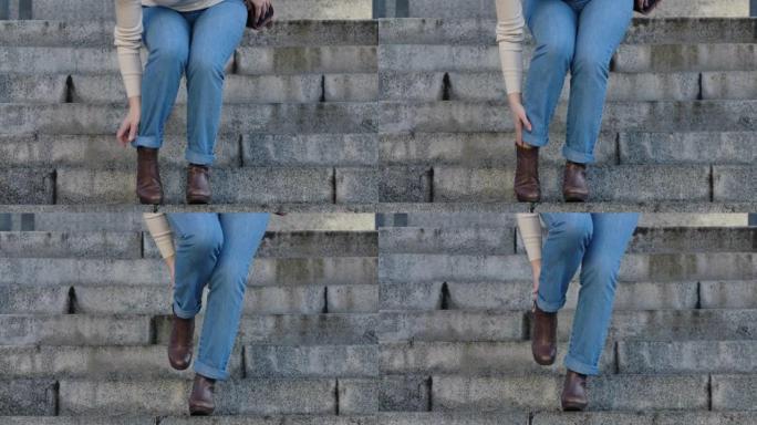 由于脚踝疼痛，女性高加索人的腿走下楼梯并停下来的特写镜头。穿着牛仔裤和棕色靴子的女人患有高跟鞋。医疗