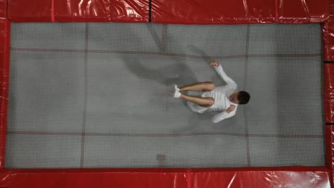 穿着白色的顶级体操运动员杂技演员的景色在蹦床上进行翻筋斗
