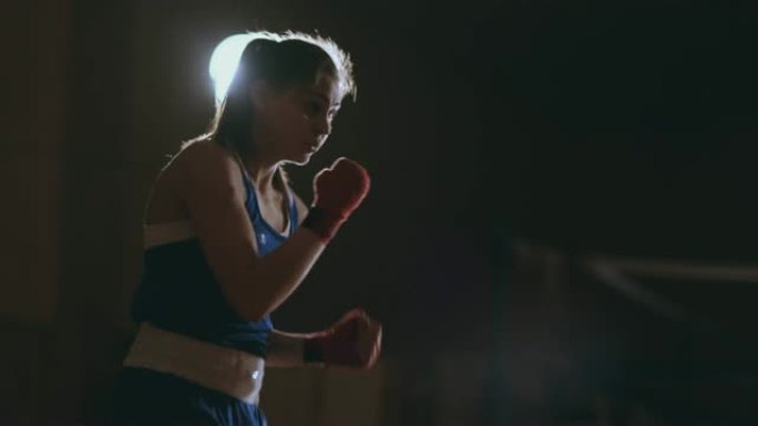 专业美丽的女拳击手穿着蓝色衣服，手腕上有红色绷带，在一个黑暗的大厅房间里慢动作地进行一场影子搏斗。s