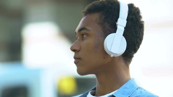 沮丧的美国黑人少年男孩戴着耳机听音乐，忧郁