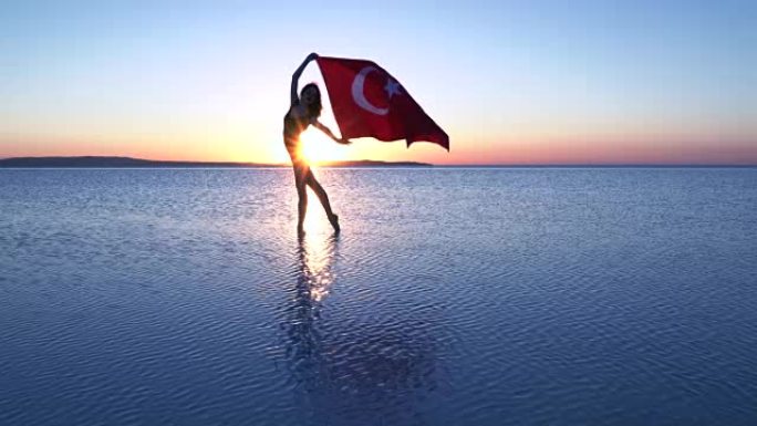 美丽的芭蕾舞演员在水上举着一面土耳其国旗。有风的一天。慢动作