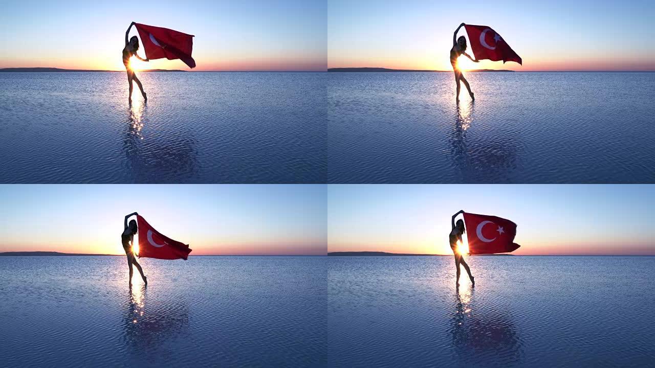 美丽的芭蕾舞演员在水上举着一面土耳其国旗。有风的一天。慢动作