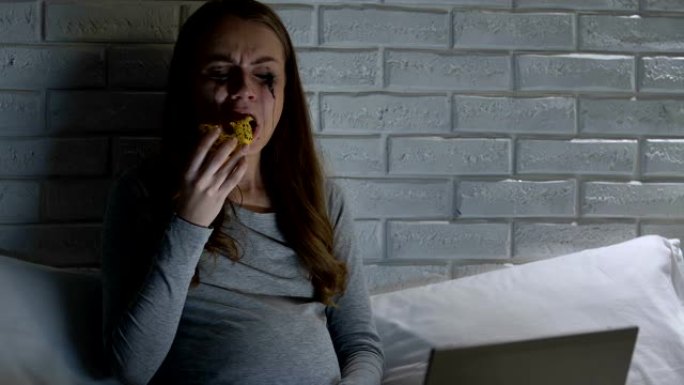 深深的哭泣孕妇晚上在笔记本电脑前吃甜甜圈，问题