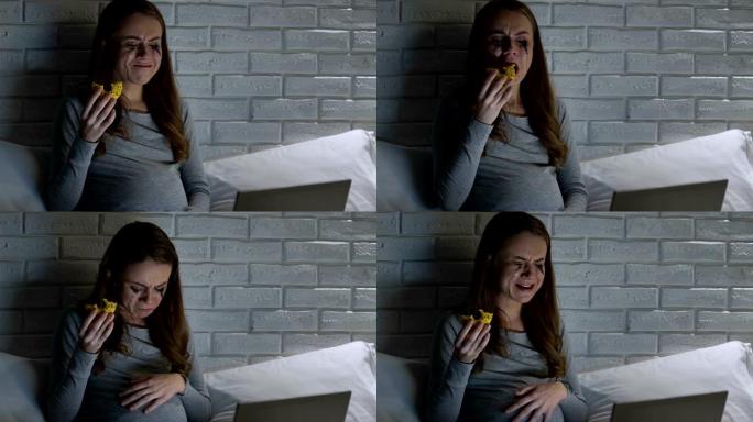 深深的哭泣孕妇晚上在笔记本电脑前吃甜甜圈，问题