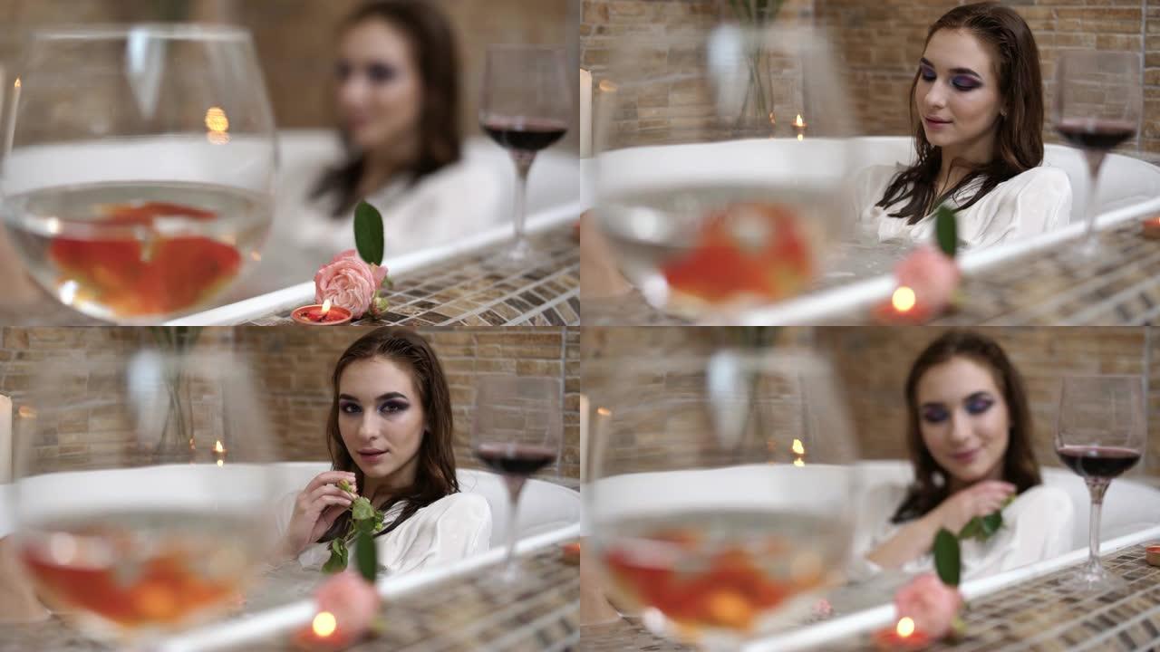 玻璃上有红色的鱼在浴缸边缘特写。女人躺在浴缸里拿着小玫瑰