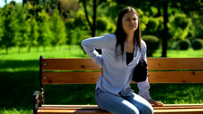 剧烈背痛的女人坐在公园的长凳上休息，被动的生活方式