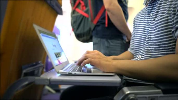 年轻人正在飞机上的笔记本电脑上工作