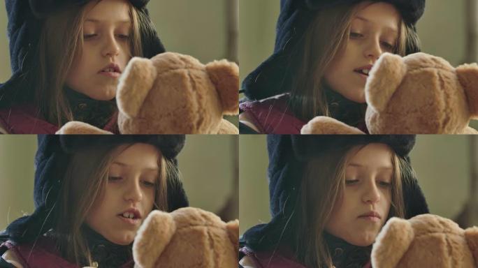 一个可爱的无家可归的女孩戴着带耳罩的帽子和米黄色的泰迪熊说话的肖像