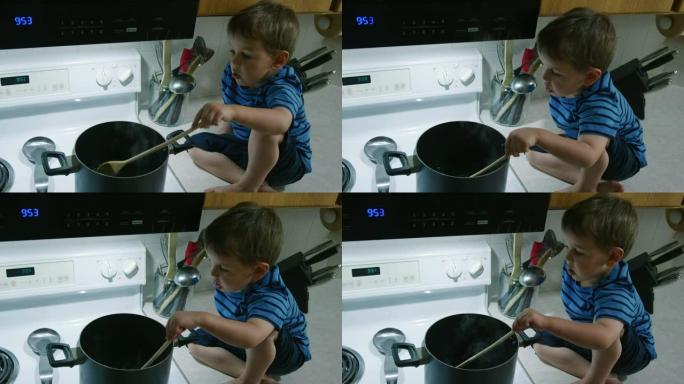 一个三岁的白人男孩坐在厨房的柜台上，在一个大锅里搅拌液体，这是坐在炉顶的炉灶