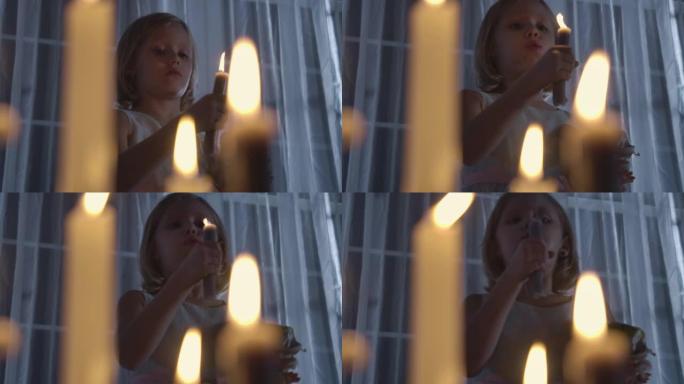 白人女孩拿着洋娃娃吹蜡烛的肖像。晚上站在大窗前的烛光下的怪异孩子。恐惧，恐惧，奇怪。