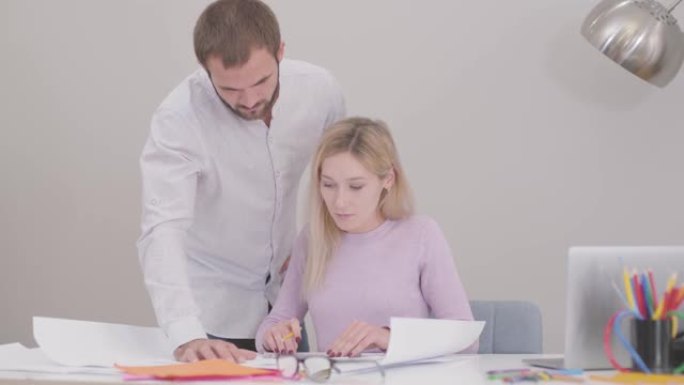 两位白人设计师改进办公室的蓝图。年轻的男人和女人翻阅图纸，女建筑师在纸上实现想法。工作场所的专业人士