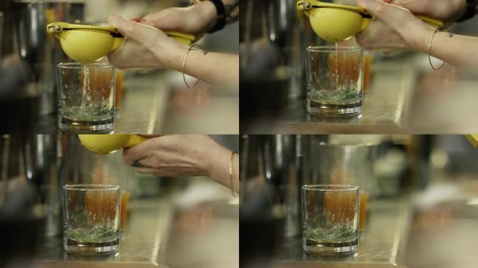 一名高加索女性调酒师在酒吧制作鸡尾酒时，使用柠檬榨汁机厨房工具将柠檬汁挤入透明的威士忌杯中