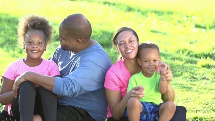 有两个孩子坐在草地上的快乐黑人家庭