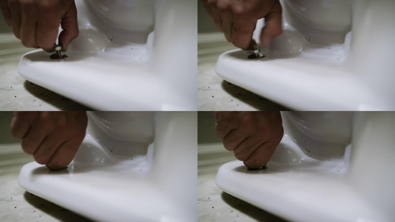 一名高加索修理工将螺母放在法兰螺栓上，然后用手指将其拧紧，以将瓷质马桶固定在室内家用浴室的地板上