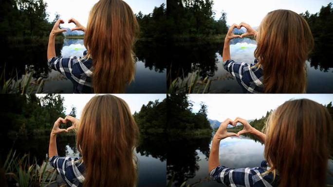 站在湖边的年轻女子在风景上制作心形手指框