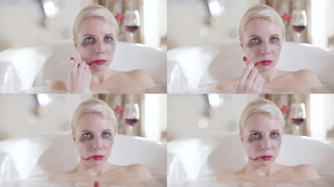 金发女人在脸颊上涂上红色唇膏，看着相机的特写镜头。沮丧的疯狂白人女士在浴缸里摆姿势的肖像。疯狂，绝望