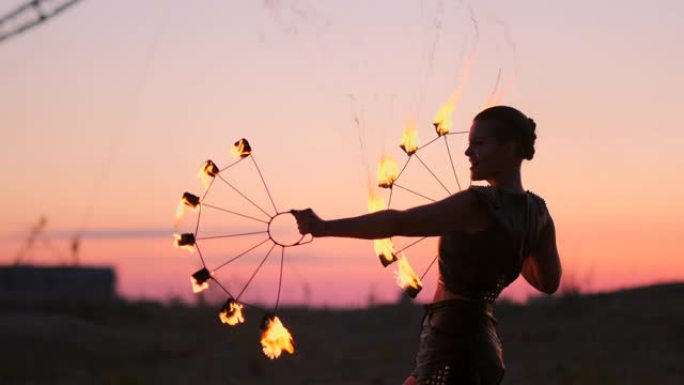 烈火舞者在日落时。一名年轻女子在舞蹈表演中与火圈对着日落摆姿势。