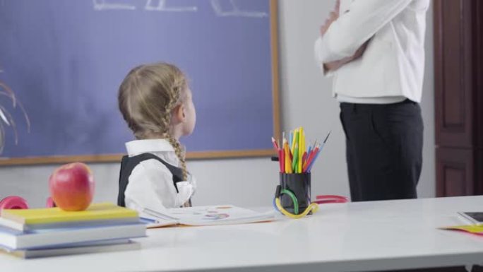 小高加索女学生的肖像回头看黑板，转身对着镜头，把头放在手上。面目全非的女人教疲惫的孩子。智力，教育。