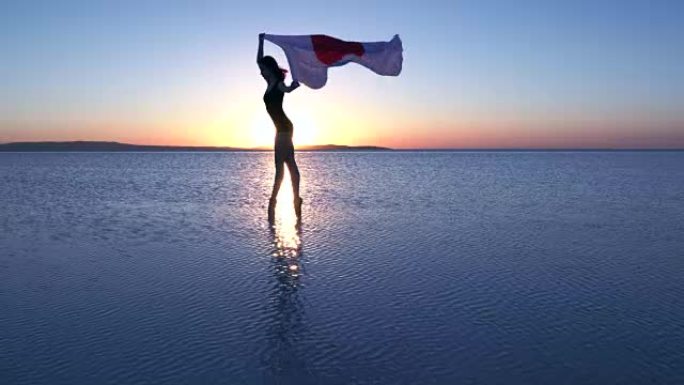 美丽的芭蕾舞演员在水上举着一面日本国旗。有风的一天。